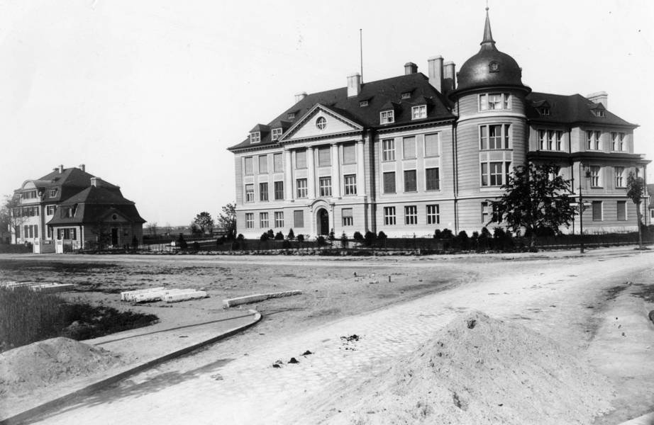 Historisches Verwaltungsgebäude mit klassizistischen Elementen, hohem Turm und mehreren Fenstern umgeben von unbefestigten Straßen.