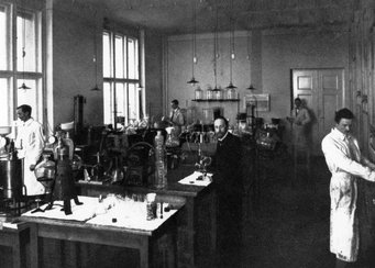 Willstätters Labor um 1912, Richard Willstätter in der Mitte; Foto: Archiv der Max-Planck-Gesellschaft Berlin-Dahlem Historisches Chemielabor mit Forschenden, zahlreichen Glasgefäßen und Apparaturen, beleuchtet von großen Fenstern.