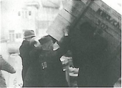 In einer historischen Schwarz-Weiß-Aufnahme heben zwei uniformierte Männer eine große Kiste oder einen Behälter, vermutlich bei einer Arbeitssituation im Freien.