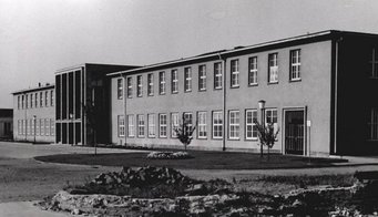 Das ehemalige Hauptgebäude des MPI für Chemie auf dem Universitätscampus in Mainz. Bild: MPI für Chemie Schwarz-weiß-Fotografie eines zweistöckigen Gebäudes mit vielen Fenstern, zwei kleinen Bäumen und einer Lampe im Vorgarten, umgeben von einer unbefestigten Fläche.