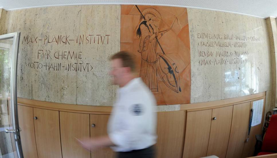 Innenaufnahme eines Flurs mit Wandinschrift des Max-Planck-Instituts für Chemie, einem künstlerischen Wandbild und einer unscharfen Person im Vordergrund.