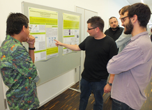 Wissenschaftliche Diskussion während des Postertags, der einmal pro Jahr stattfindet. Personen vor einem Poster