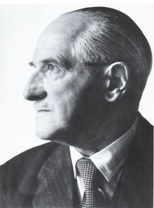 An older man in a suit and tie, photographed from the side, with the focus on his head and shoulders.