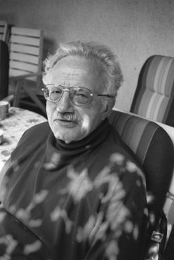 Elderly person sitting on a striped chair indoors.