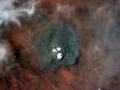Der Rauch eines Feuers in extrem trockener Vegetation ist fast schwarz. Das Bild entstand am 17. Januar 2013 in der Great Victoria Wüste, Australien. Eine helle Kumuluswolke steigt von der Spitze der Rauchwolke auf.