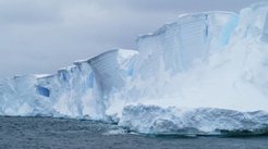 White icebergs with jagged surfaces tower over dark waters, set against a grey, overcast sky.