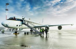 Airplane on the runway with staff descending stairs, cloudy sky above.
