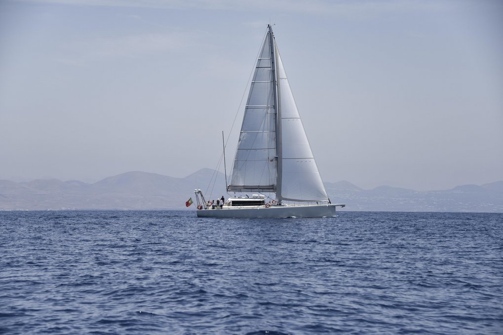 Sailboat with raised sails on calm sea near distant mountains.