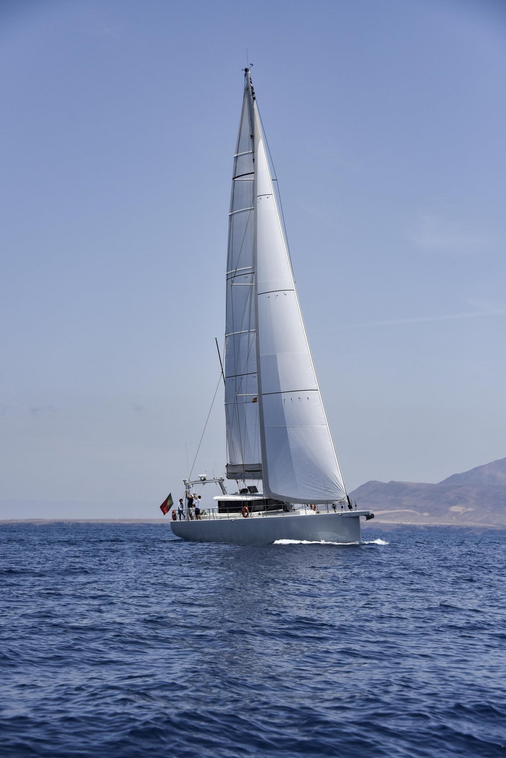 White sailboat sailing on calm blue sea with distant hills in the background.