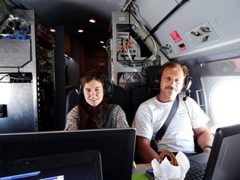Mira Pöhlker on board the HALO research aircraft together with Tommy Leder (DLR), monitoring data acquisition. Photo: Sergej Molleker Mira Pöhlker (on the left) and Tommy Leder (on the right) with headsets seated in an aircraft cockpit, surrounded by technical equipment.