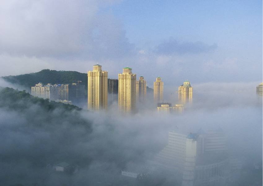 Hochhäuser ragen aus dichtem Nebel in einer städtischen Landschaft hervor.