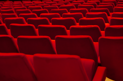 Empty red theater seats aligned in rows, viewed from the back.