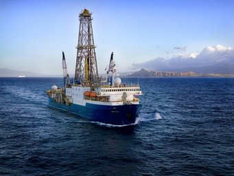 Researchers analysed a 169-metre-long sediment core collected at the bottom of the Southern Ocean by the research vessel JOIDES Resolution, in conjunction with the International Ocean Drilling Project (IODP). © IODP A research vessel equipped with a prominent drilling tower moves through open waters, with a mountainous coastline and scattered clouds in the background.