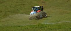 Tractor with spray tank disperses liquid over grassy field under clear sky.