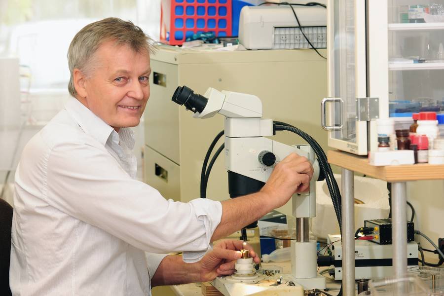 Laboratory scene with researcher Mikhail Eremets using a microscope to examine samples on a table filled with various equipment.