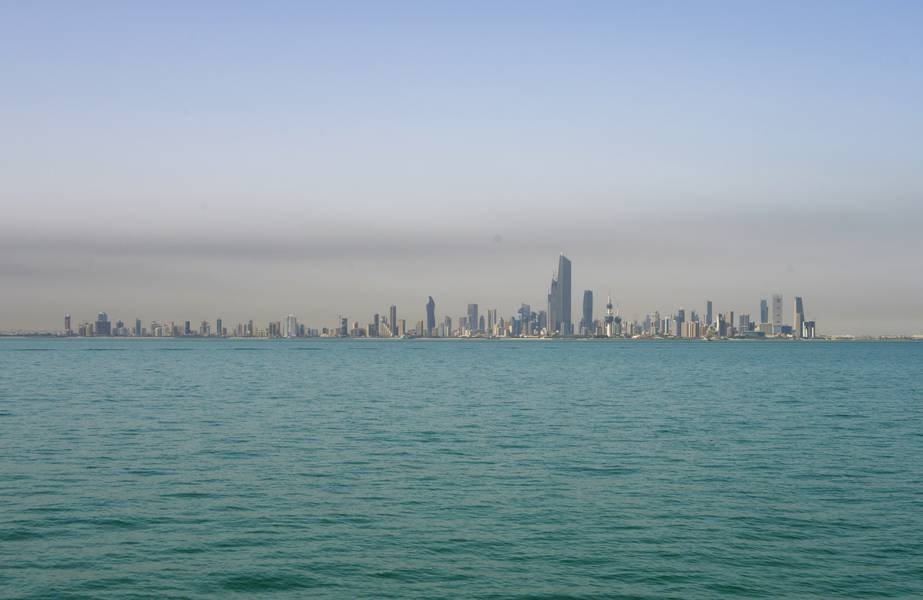 City skyline with numerous skyscrapers seen across a body of water under a clear sky.