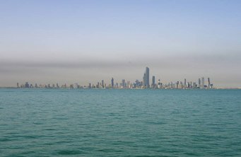 Die Dunstglocke über Kuwait ist vom Schiff aus gut sichtbar. Foto: MPIC Skyline von Kuwait-Stadt über das Meer bei klarem Himmel.