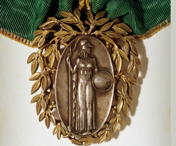 Bronze medal depicting a standing figure with a spear and shield, encircled by a gold laurel wreath attached to a green fabric ribbon.