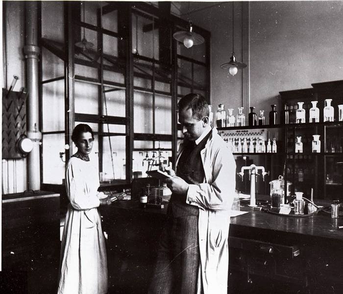 Two scientists in lab coats working in a laboratory with glassware and chemicals.