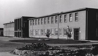 A former barracks building in Mainz became the main building of the MPI for Chemistry in 1949. Source: MPI for Chemistry Black-and-white photo of a two-story institutional building featuring rows of windows and a small landscaped area with trees and a lamp post.