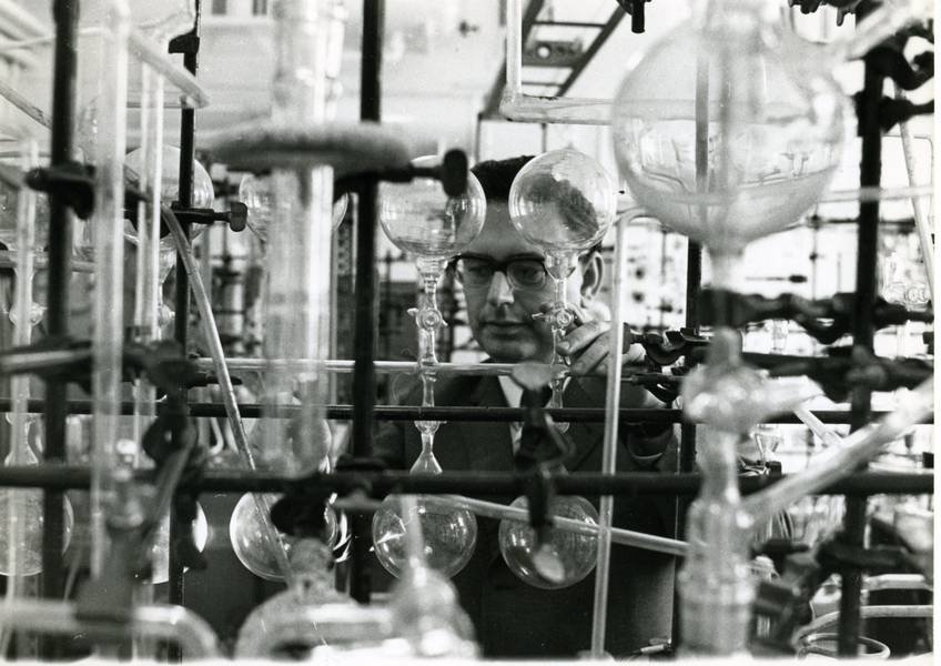 Various laboratory glass apparatuses including flasks and tubes set up on metal stands in a scientific research environment.