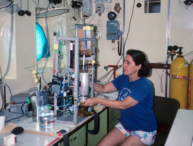 Female researcher adjusting laboratory instruments on a table with various scientific devices and gas cylinders.