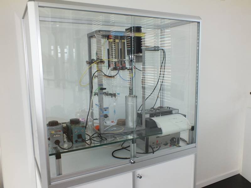 Laboratory equipment with electronic components and a printer inside a glass cabinet.
