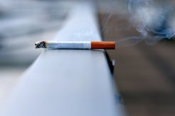 Burning cigarette with smoke rising, placed on a metal railing.