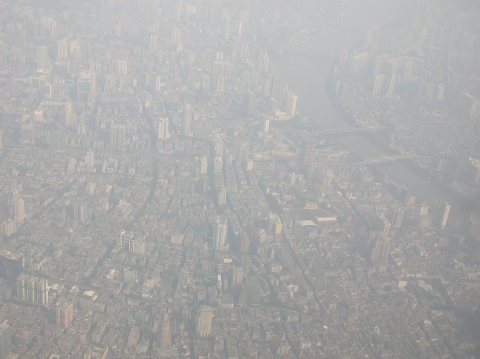 Aerial view of a city in thick smog, with many high-rise buildings and a river visible.