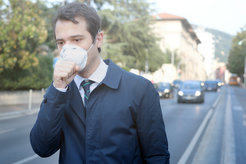 Mann in dunklem Mantel mit Krawatte auf einer städtischen Straße. Er trägt eine FFP3-Maske