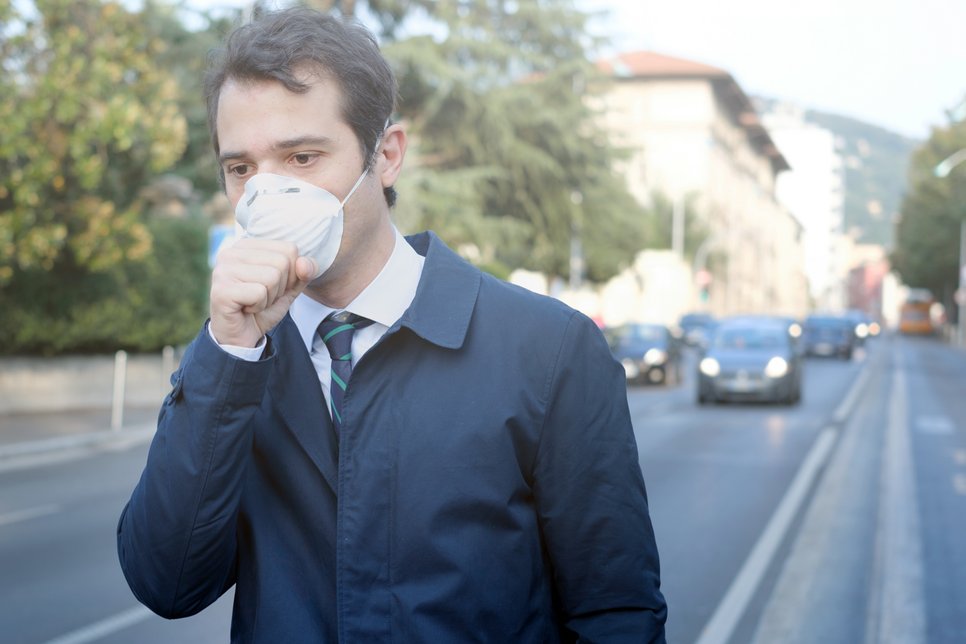 Mann in dunklem Mantel mit Krawatte auf einer städtischen Straße. Er trägt eine FFP3-Maske