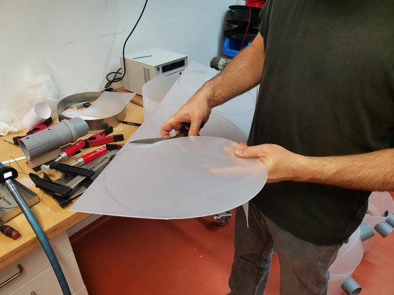 Mann schneidet kreisförmiges Stück aus transparenter Kunststofffolie auf Werkbank.