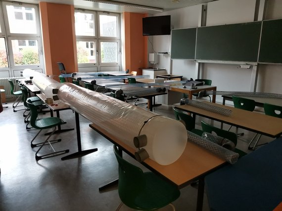 Klassenzimmer mit leeren Tischen und verpackten Rollen.