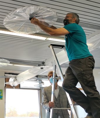 A simple exhaust air system for classrooms: Thomas Klimach assembles one of the hoods that will collect the warm air exhaled by students above a desk and direct it into the exhaust air duct. Also present: Roland Wollowski, Headmaster of IGS Mainz-Bretzenheim. A simple exhaust air system for classrooms: Thomas Klimach assembles one of the hoods that will collect the warm air exhaled by students above a desk and direct it into the exhaust air duct. Also present: Roland Wollowski, Headmaster of IGS Mainz-Bretzenheim.