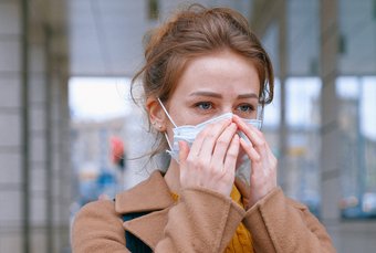 Is the mask fitting properly? In most environments, the airborne virus concentration is so low that even simple surgical masks are very effective at containing the spread of COVID-19. Provided the mask is worn properly." Young woman wearing a face mask. She is checking with her fingers to see if it fits properly.