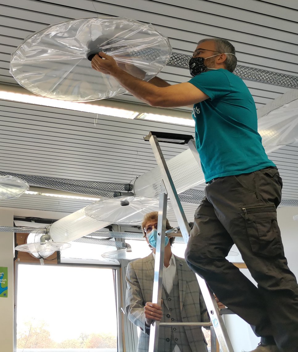 Person steht auf Leiter und befestigt eine transparente Kunststoffabdeckung an einer Deckeninstallation.