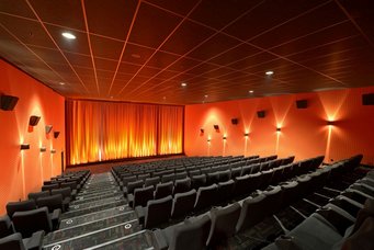 Anspannung in der Luft: Bei Nervosität geben Kinobesucher vermehrt Isopren ab - ein messbarer Hinweis darauf, wie belastend ein Film ist.  Kinoreihen (dunkelgraue Sitze), Vorhang vorne (orange), Wände rechts und links (orange), beleuchtet
