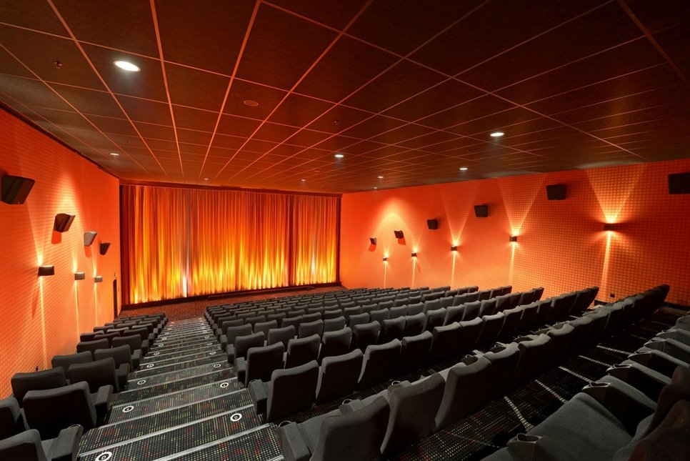 Cinema rows (gray seats) in an auditorium, curtain at the front (orange), walls on the right and left (orange), illuminated.