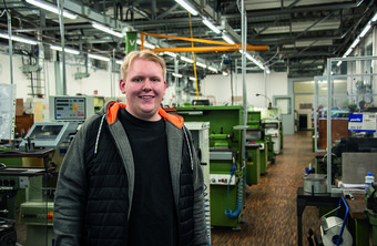 Simon Bauer, 20, angehender Feinwerkmechaniker für Geräte und Systeme Person in einer Werkstatt mit grünen Maschinen und Werkzeugen.