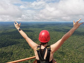Kostenfreie Bildungsmaterialien für Schüler zu Amazonasforschung erschienen. Frau mit rotem Helm, Arm in V-Form in die Luft gestreckt, auf ATTO-Turm im Amazonas stehend, von hinten zu sehen