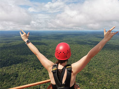 Frau mit rotem Helm, Arm in V-Form in die Luft gestreckt, auf ATTO-Turm im Amazonas stehend, von hinten zu sehen