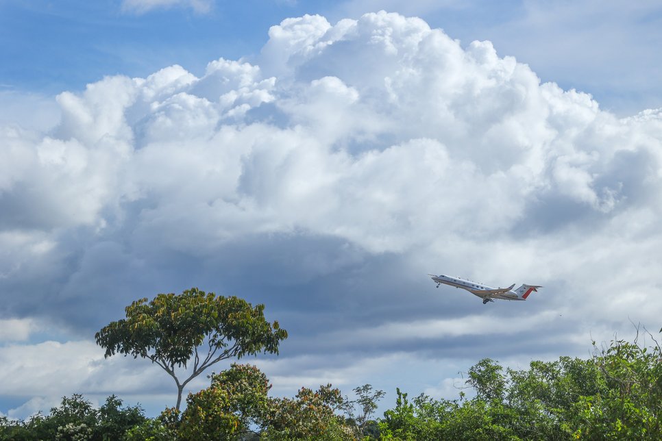 The CAFE Brazil project research aircraft shortly after takeoff.Plane ascending near lush trees under expansive clouds.