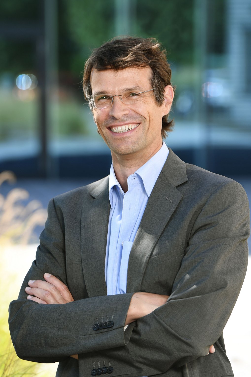 Man wearing a grey suit jacket and blue shirt with arms crossed.