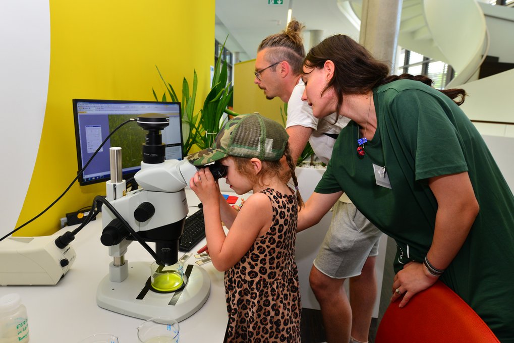 Several individuals, including a child, gathered around a table with a microscope on it.