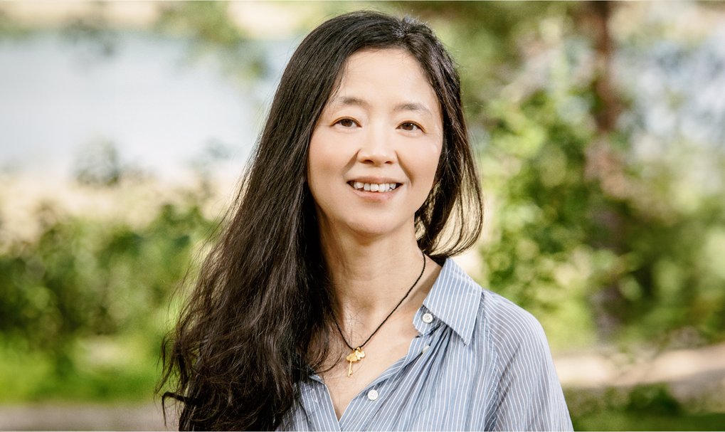 Woman with long dark hair wearing a striped shirt and a necklace outdoors.