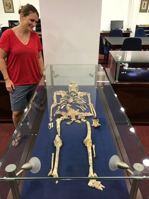 Tina Lüdecke stands beside "Little Foot," a remarkably well-preserved skeleton of Australopithecus discovered in the Sterkfontein Cave, celebrated as the most complete pre-human skeleton ever found. In her research, however, Lüdecke and her team primarily work with isolated fossilized tooth fragments.