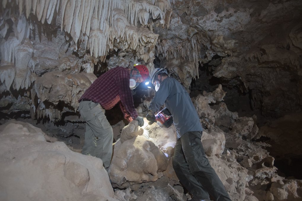 Zwei Forscher mit Helmen untersuchen eine Höhle mit Stalagmiten.