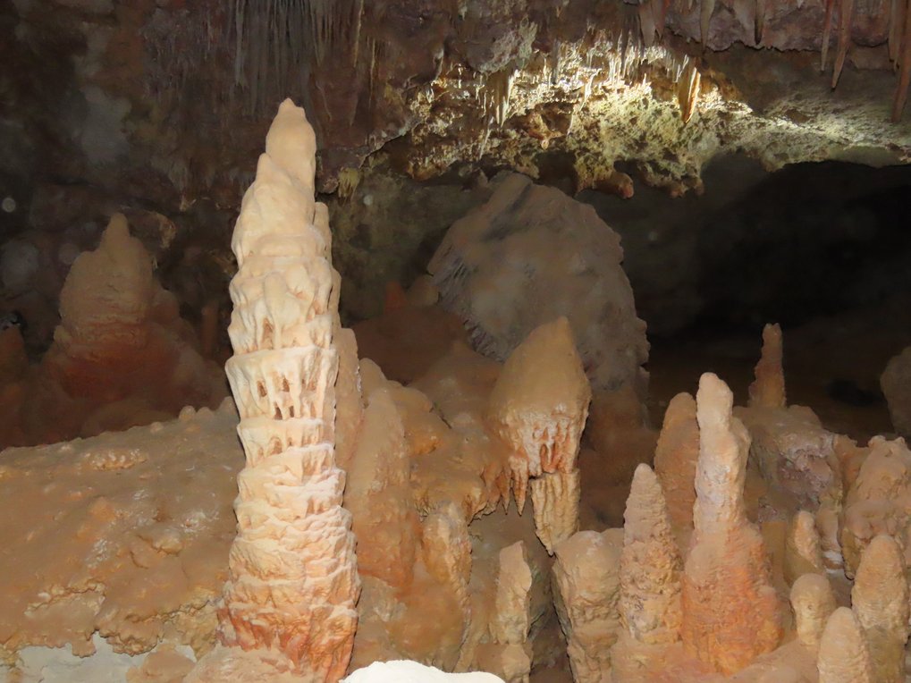 Various stalagmites rise from the cave floor, showcasing distinct orange and beige colors.