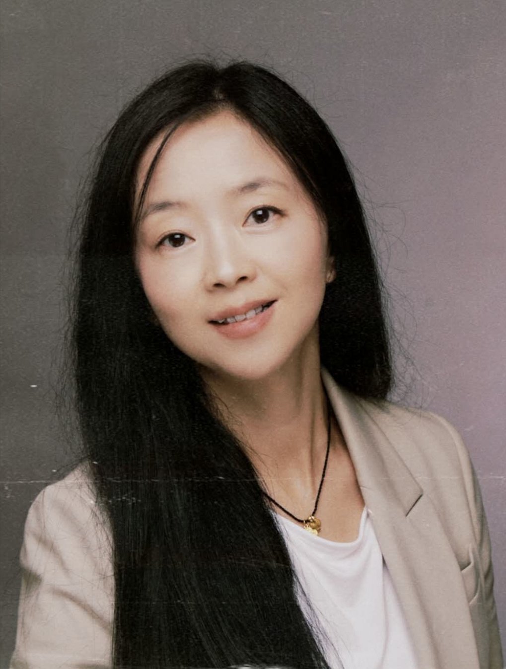 Woman with long black hair wearing a light-colored blazer and white shirt.