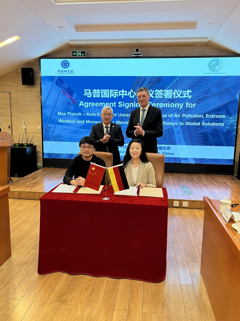 Vier Personen bei einer Vertragsunterzeichnung mit China- und Deutschlandflagge im Konferenzraum.
